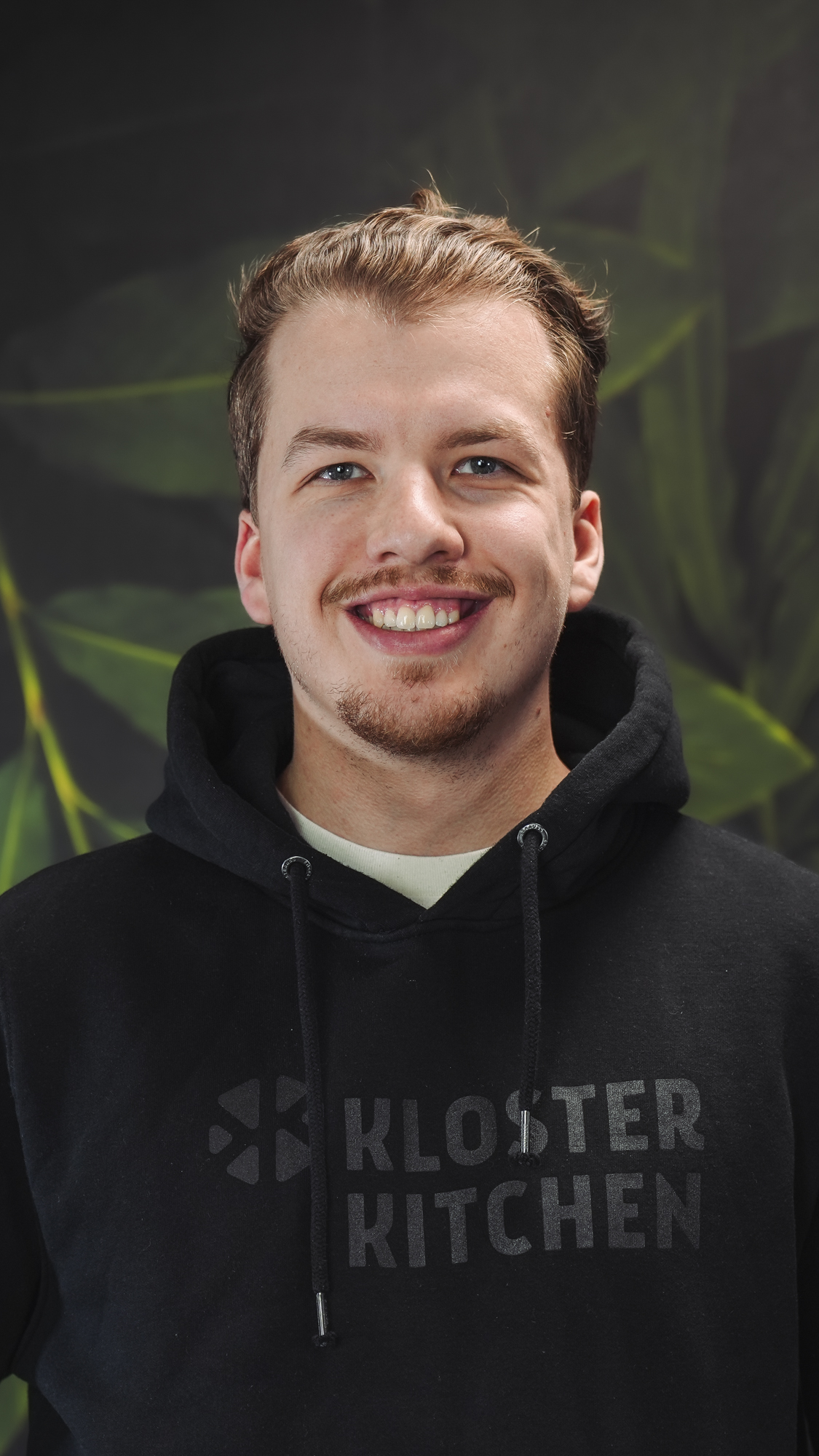 Person smiling in a black hoodie withKloster Kitchen' text.