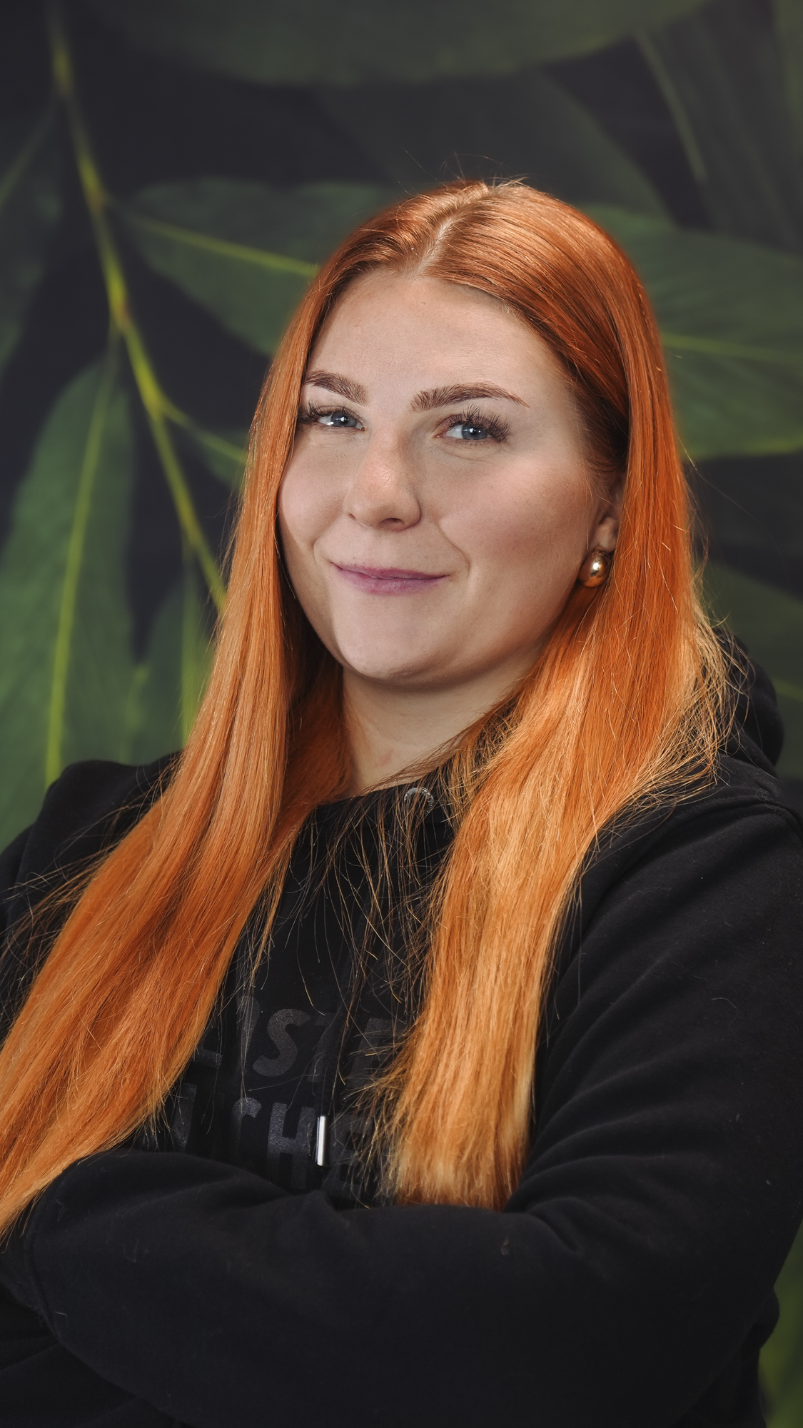A person with long red hair smiling, wearing a black hoodie.