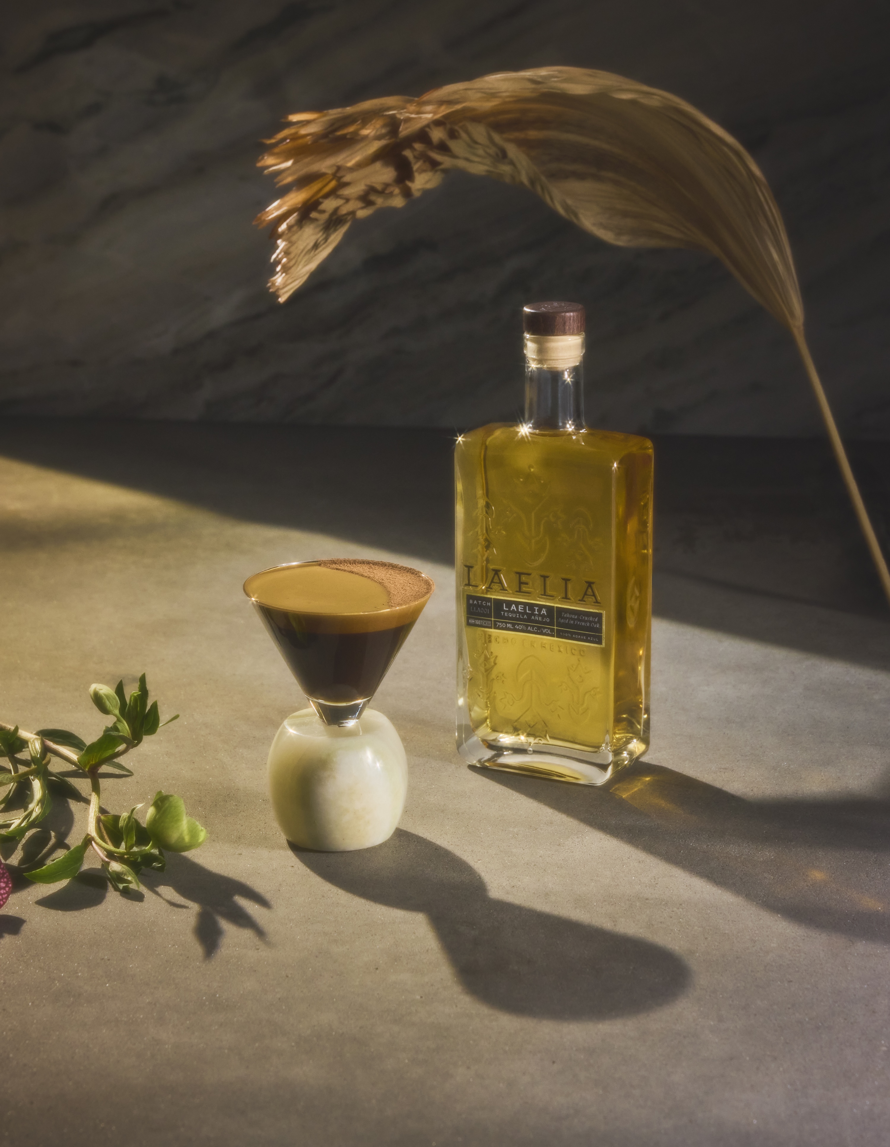 Bottle of Laelia spirit with a cocktail and decorative leaves.