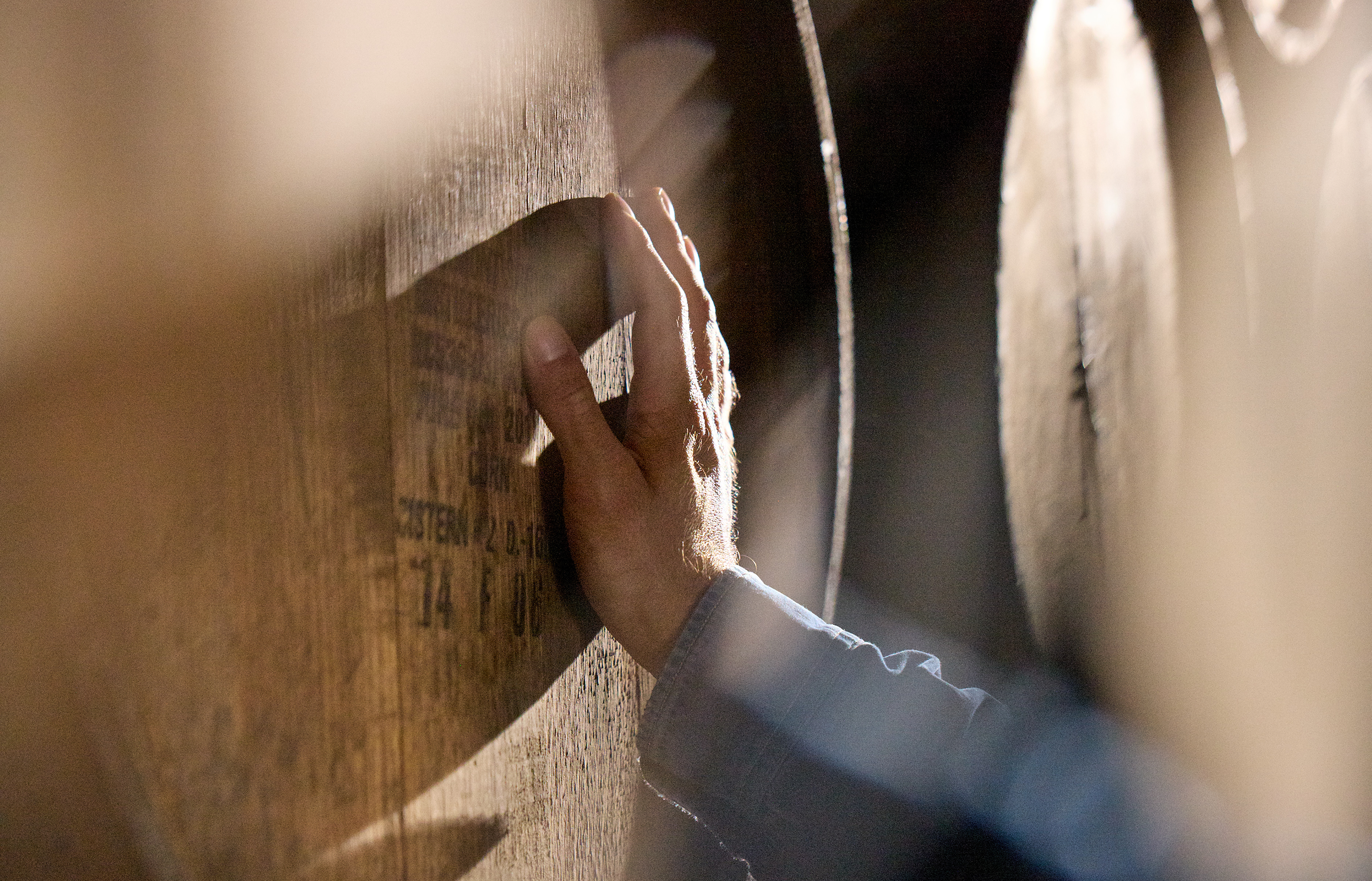 Hand touching a wooden barrel in soft lighting.