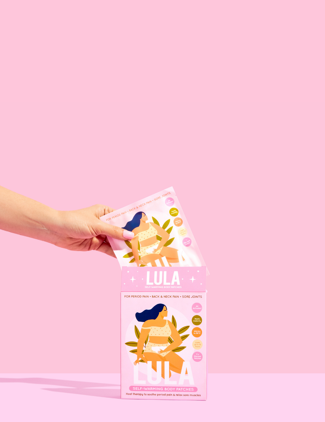 Hand holding a pack of self-warming body patches against a pink background.