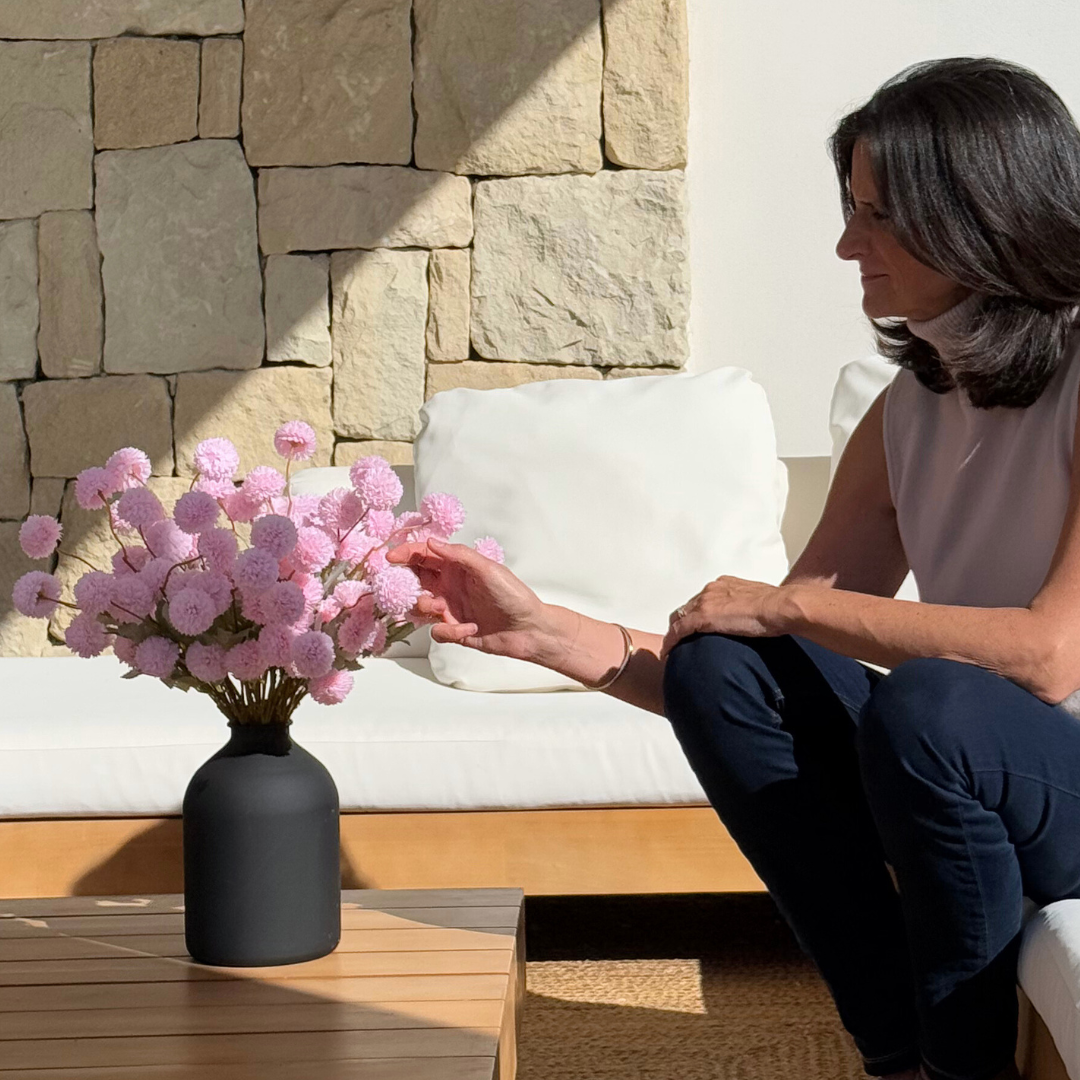 Person sitting on a couch, touching pink flowers in a black vase.
