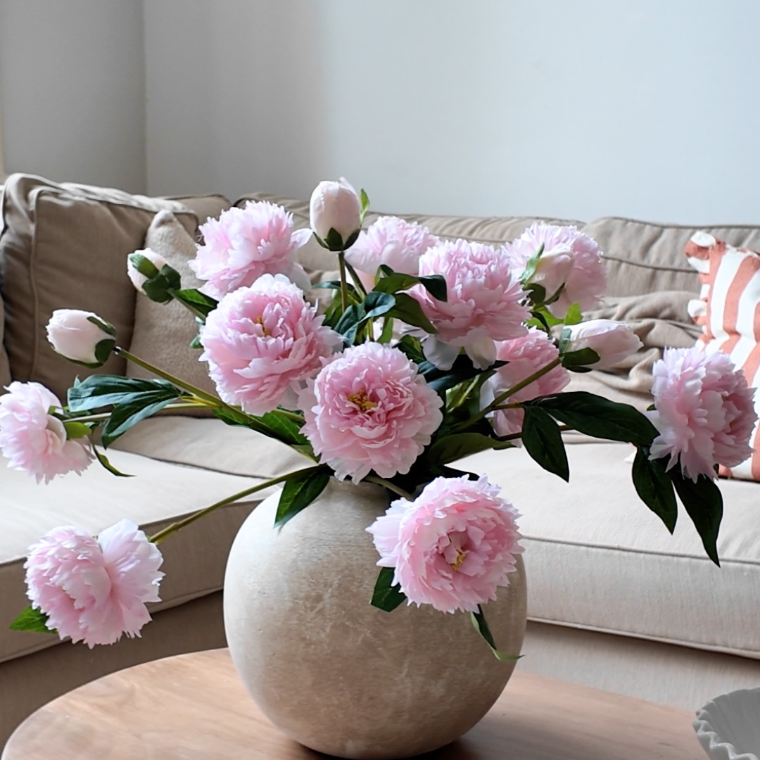 Vase of pink flowers on a table in front of a beige couch.