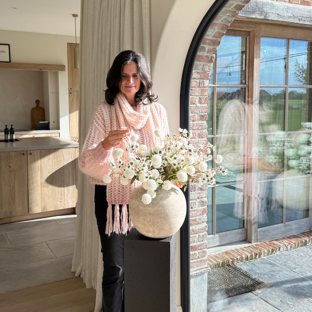 Person arranging flowers in a vase near a window with brick and glass.