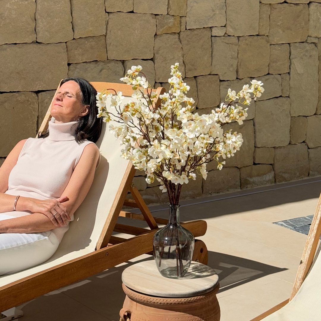 Woman relaxing on a sun lounger next to a vase of white flowers.