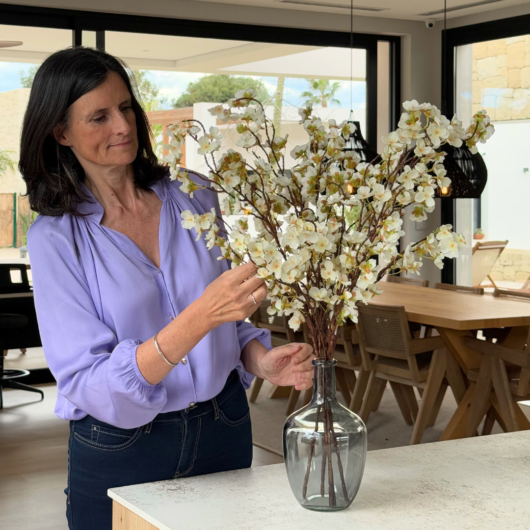 Woman arranging white flowers in a glass vase on a kitchen counter.