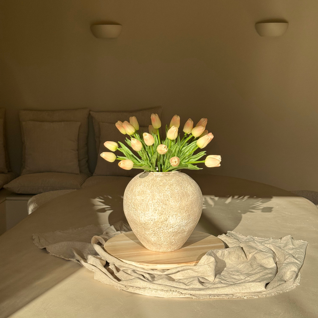 Vase with tulips on a table in a softly lit room.