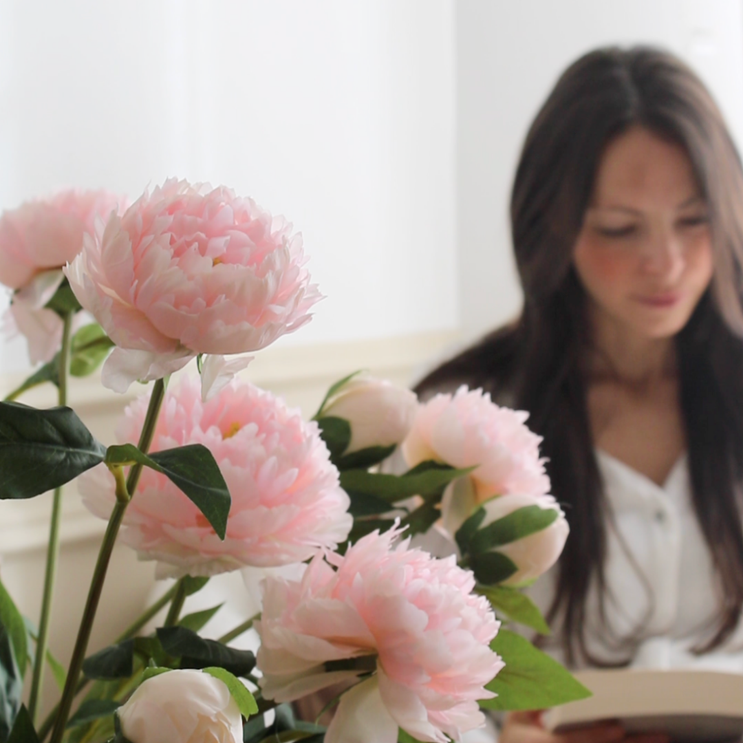 Pink peonies in focus with a person reading in the background.