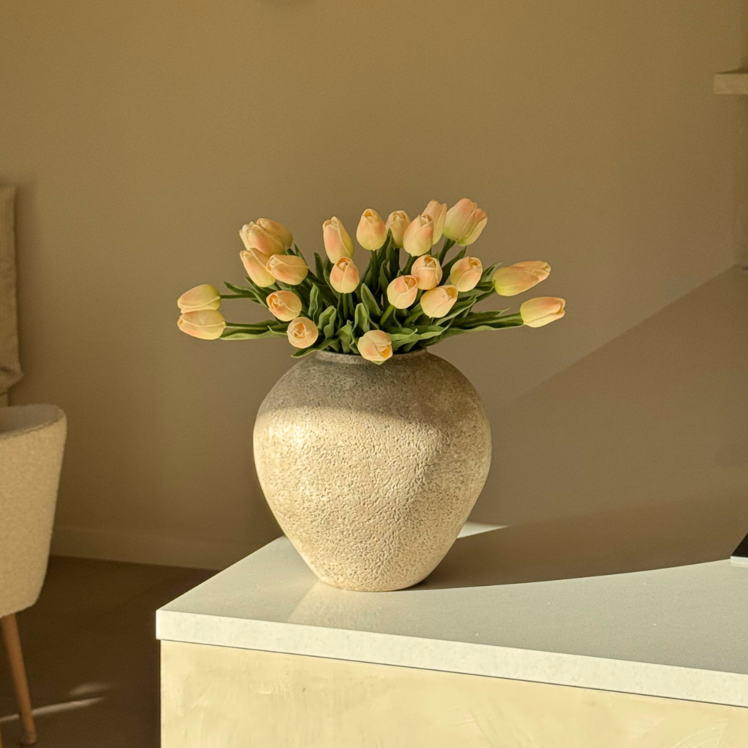 A vase of light pink tulips on a white table.