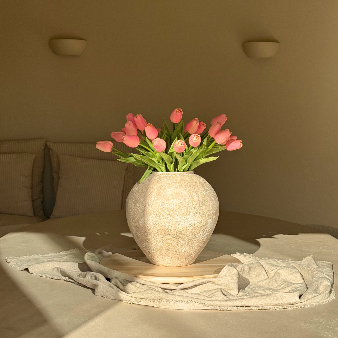 Pink tulips in a textured vase on a tablecloth-covered surface.