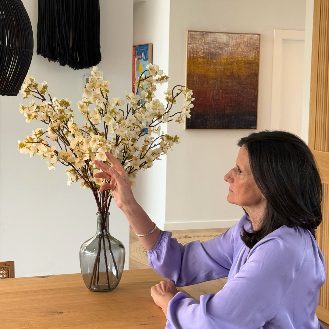 Woman in purple blouse arranging flowers in a vase on a wooden table.