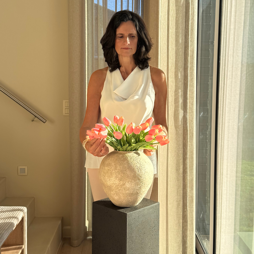 Woman arranging pink tulips in a vase near a window.
