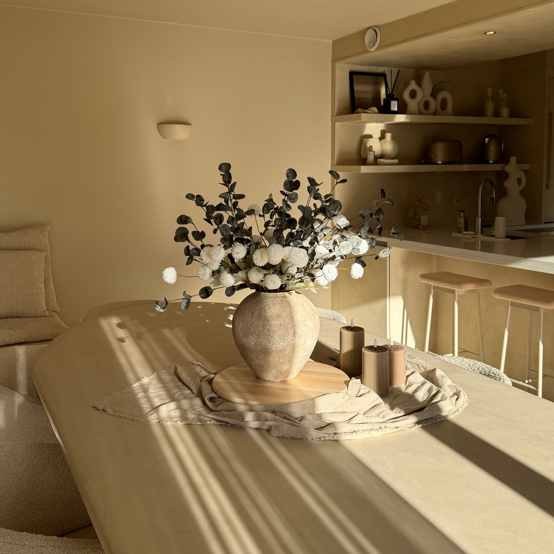 A beige room with a vase of flowers and sunlight casting shadows on a table.