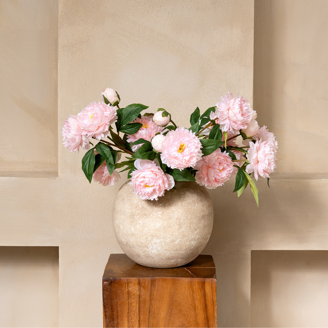 A vase with pink peonies on a wooden pedestal against a beige background.