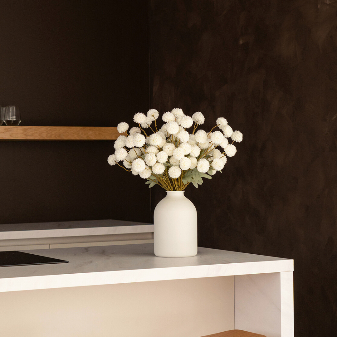 White flowers in a white vase on a marble countertop.