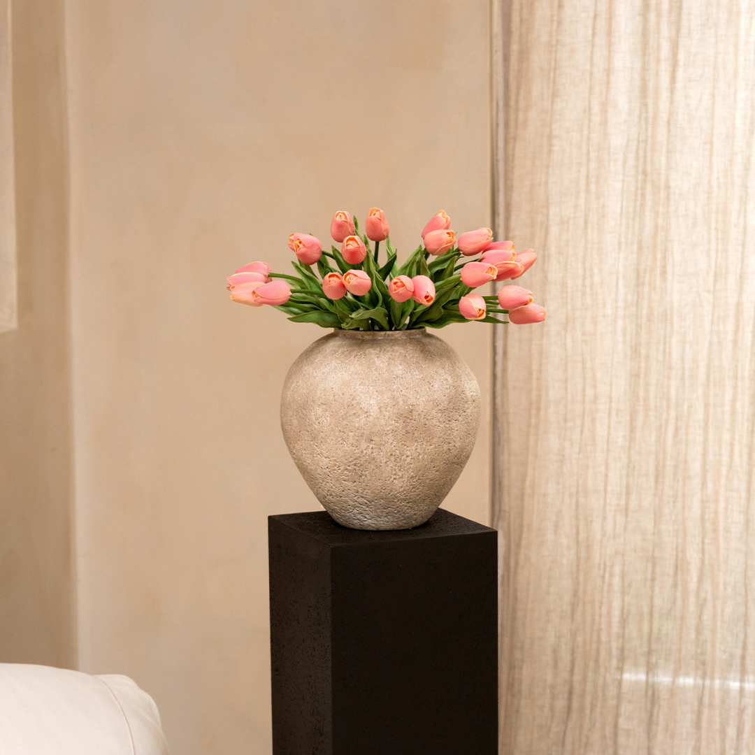 Pink tulips in a textured vase on a black pedestal.