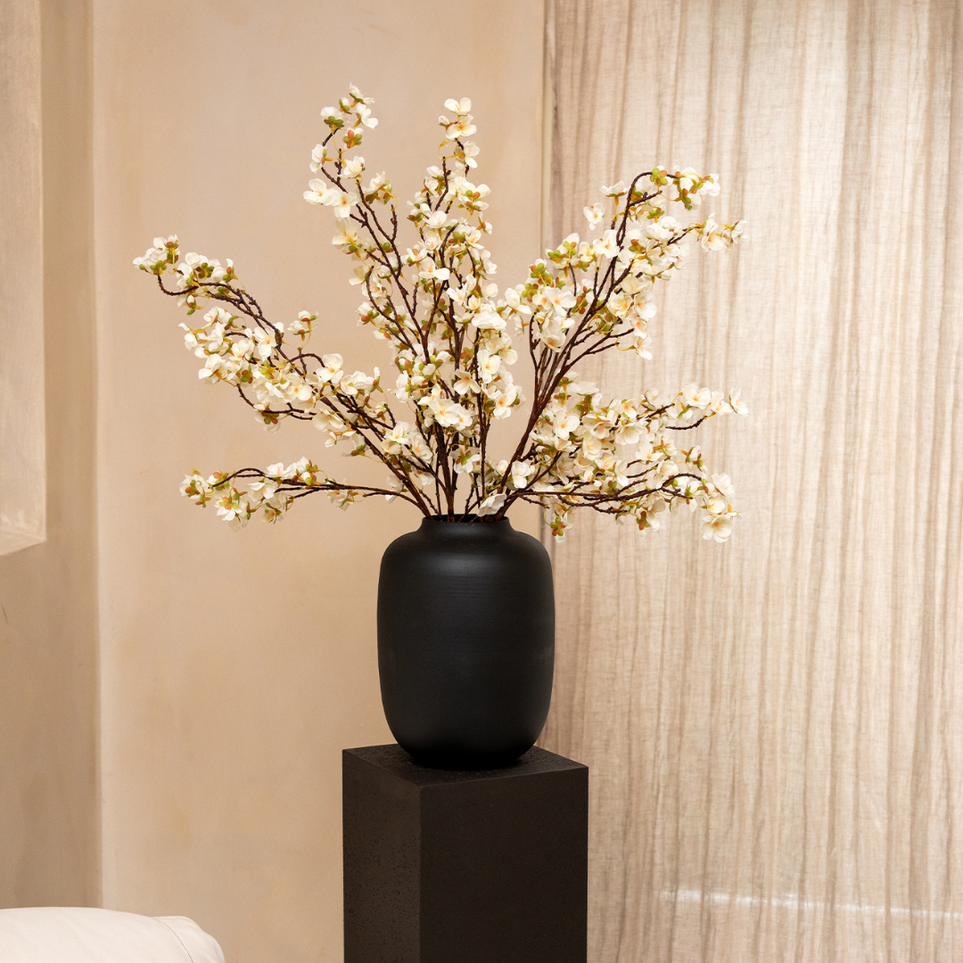 White flowering branches in a matte black vase sitting on a black pedestal.