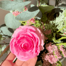 A bouquet of pink and cream flowers with eucalyptus in a textured white vase on a stool.