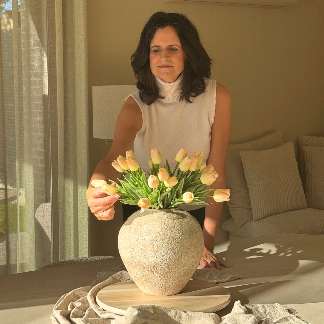 Person arranging pink tulips in a large vase on a table.