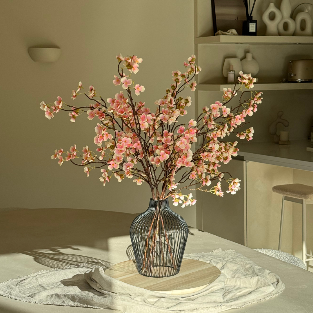 Pink cherry blossoms in a wire vase on a table.