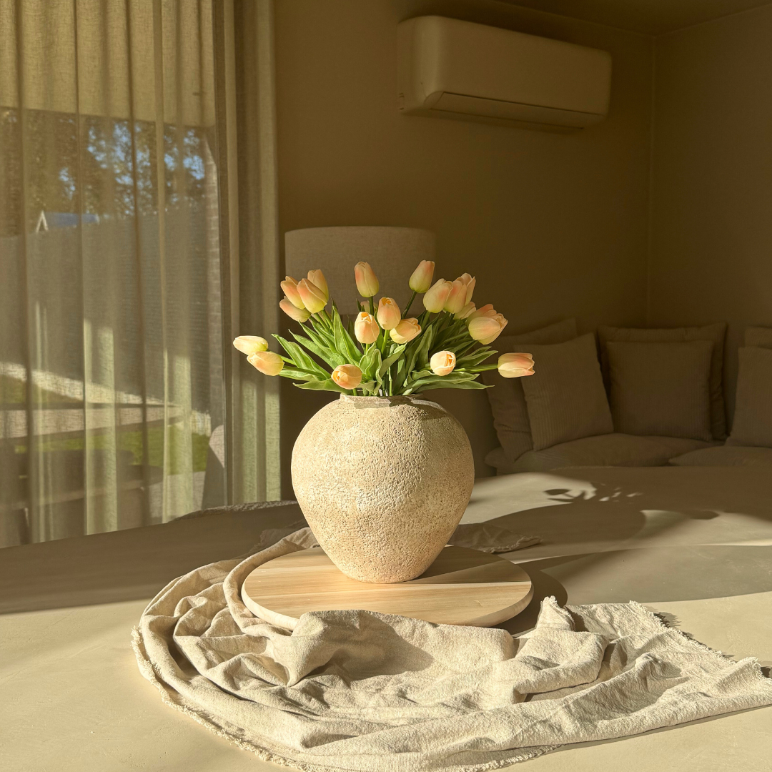 Vase of tulips on a wooden table in a sunlit room.