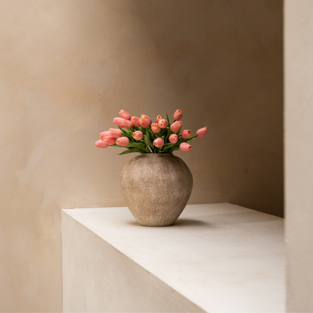 A stone vase with pink tulips on a beige ledge.