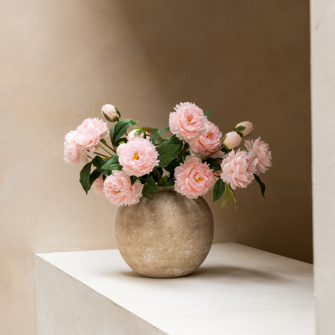 Vase with pink flowers on a white ledge against a beige wall.