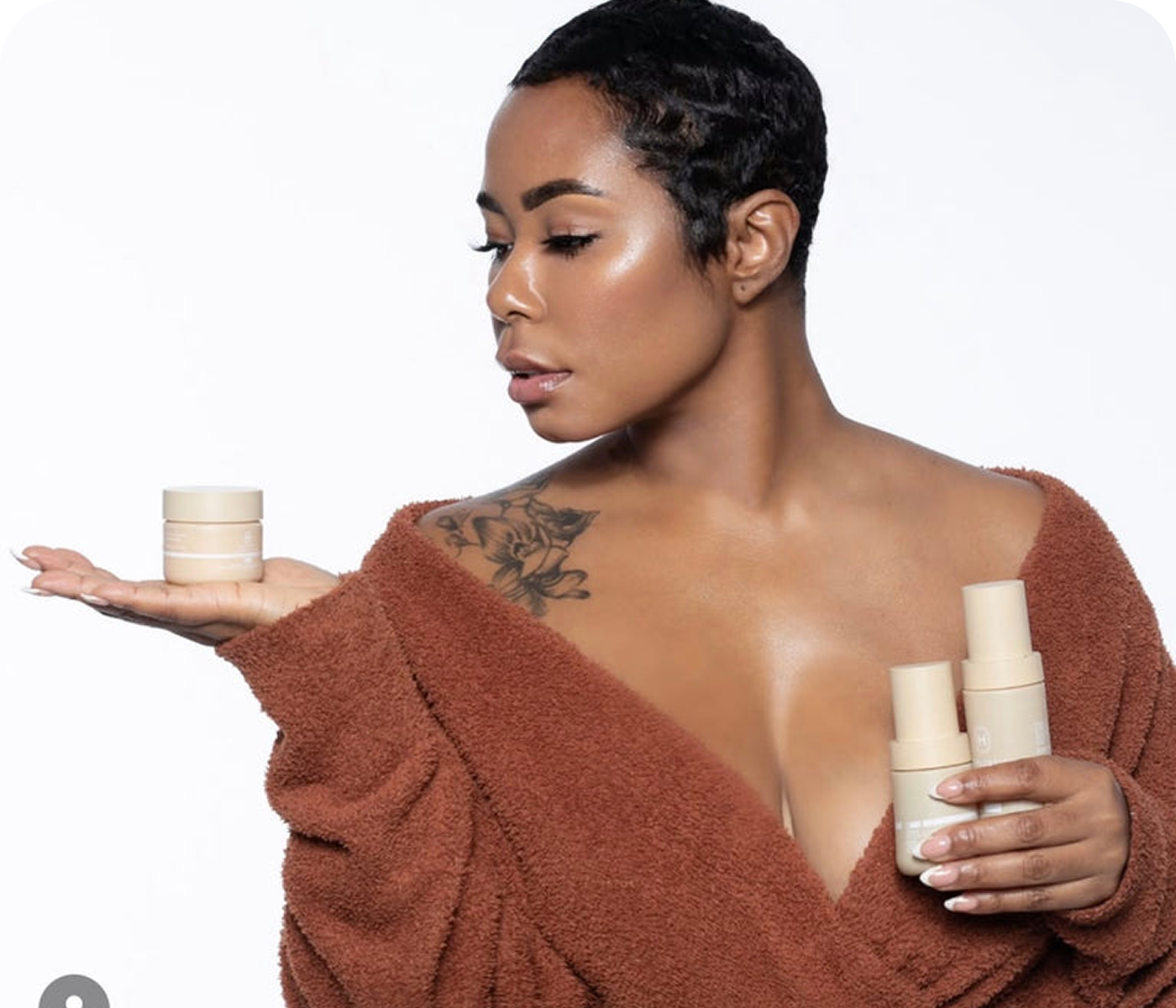 Person in brown robe holding skincare products against a white background.