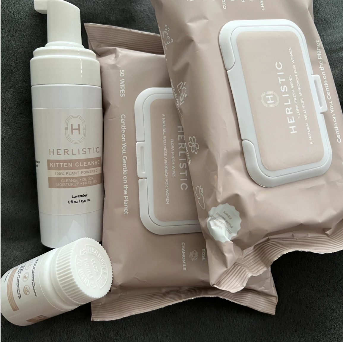 Herlistic skincare products including wipes and a cleanser bottle on a dark surface.