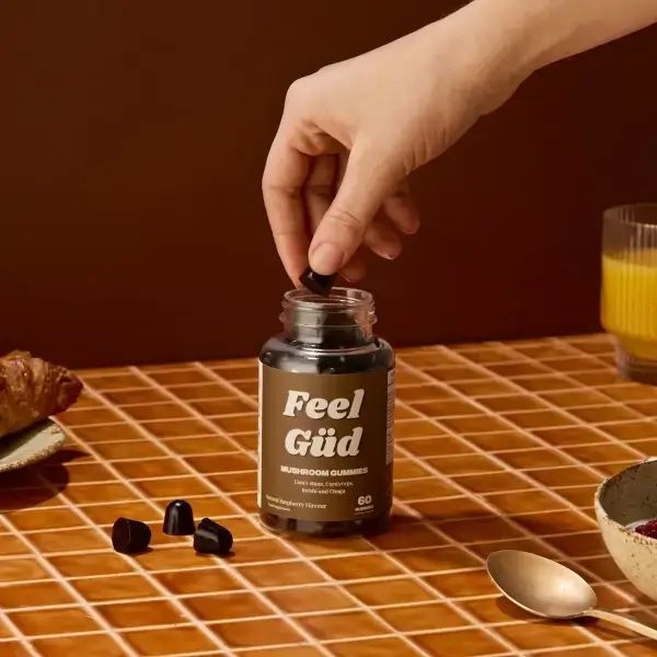 Hand picking a gummy from a jar labeled 'Feel Güd' on a tiled table.