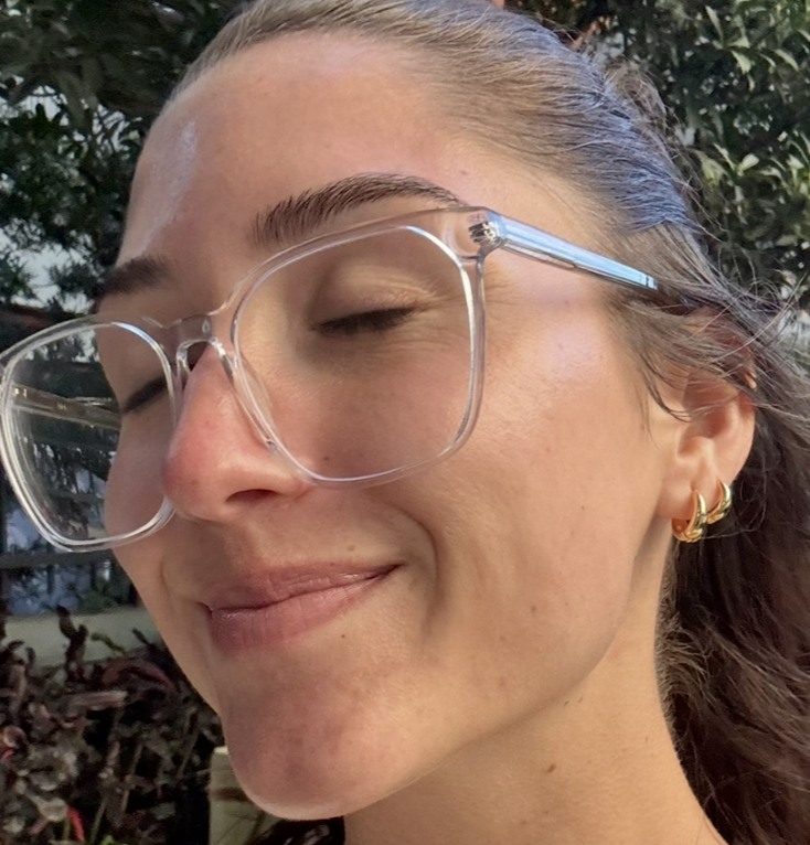 Person with glasses smiling, eyes closed, outdoors.