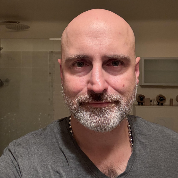 A close-up photo of a bald man with a gray beard and a slight smile, wearing a gray t-shirt.