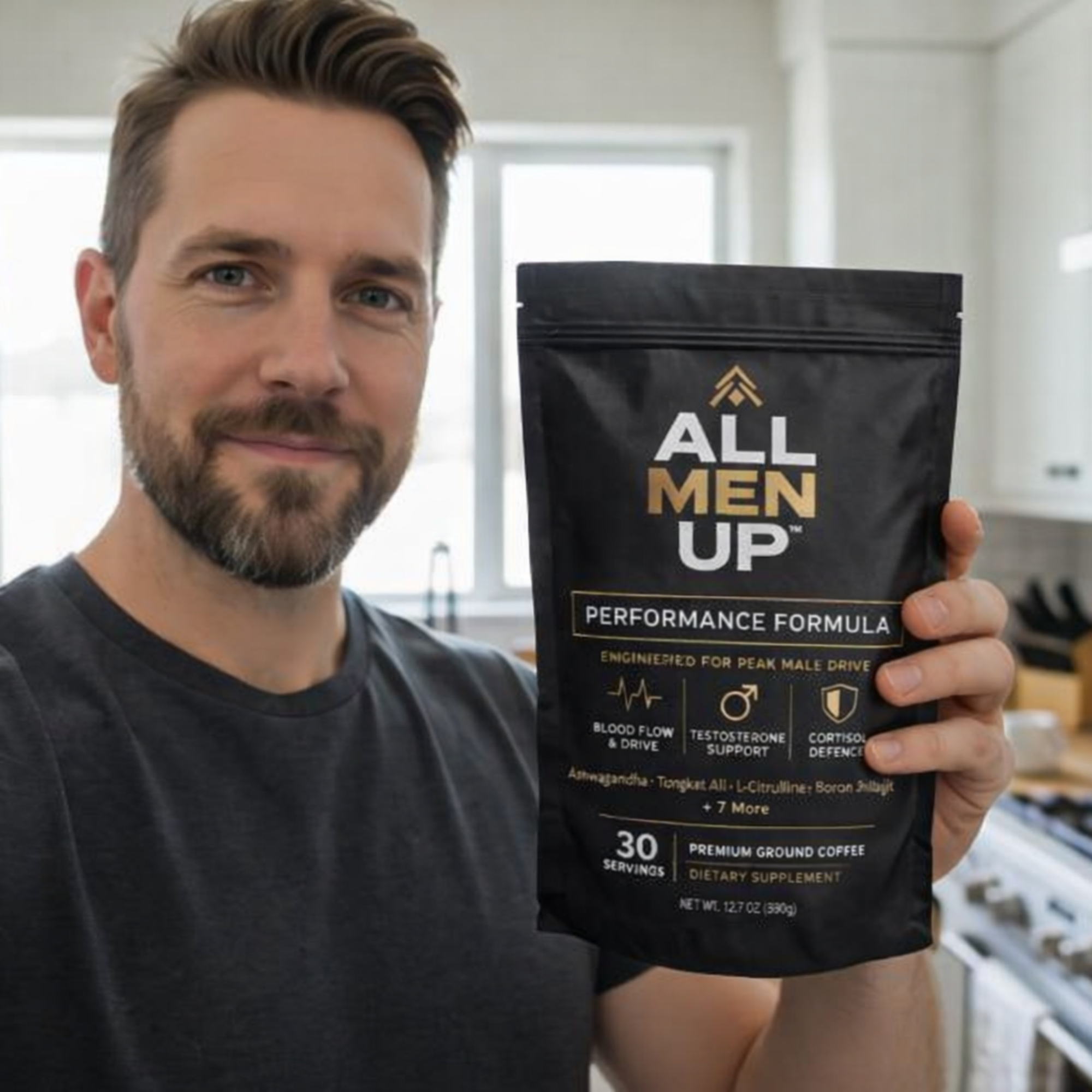 A smiling man with a beard holds up a black bag of All Men Up coffee supplement.