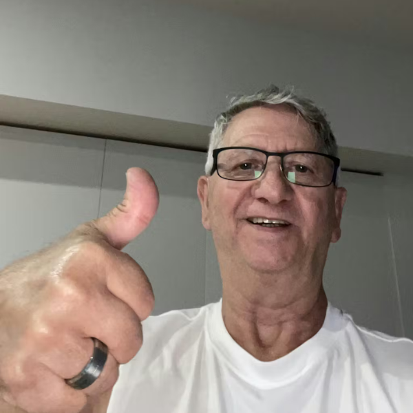 A smiling older man with gray hair and glasses gives a thumbs up to the camera.