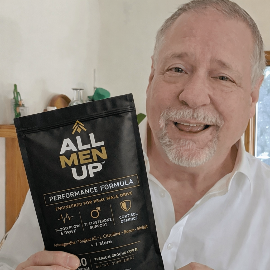A smiling man holds up a black pouch of All Men Up performance formula coffee.