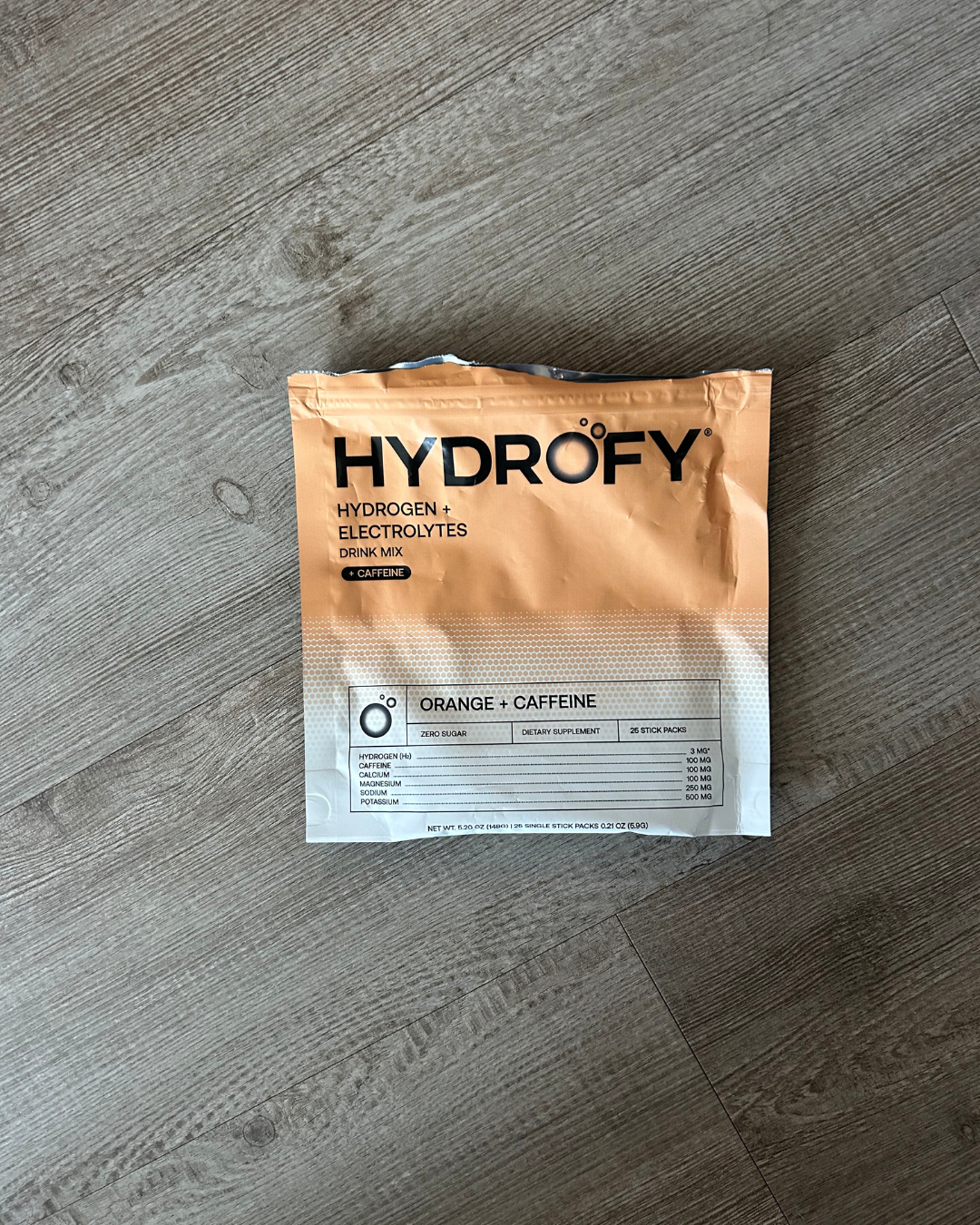 Orange and white Hydr8 hydrogen electrolytes drink mix packet on wooden floor.