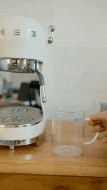 Person placing a glass mug under a white espresso machine.