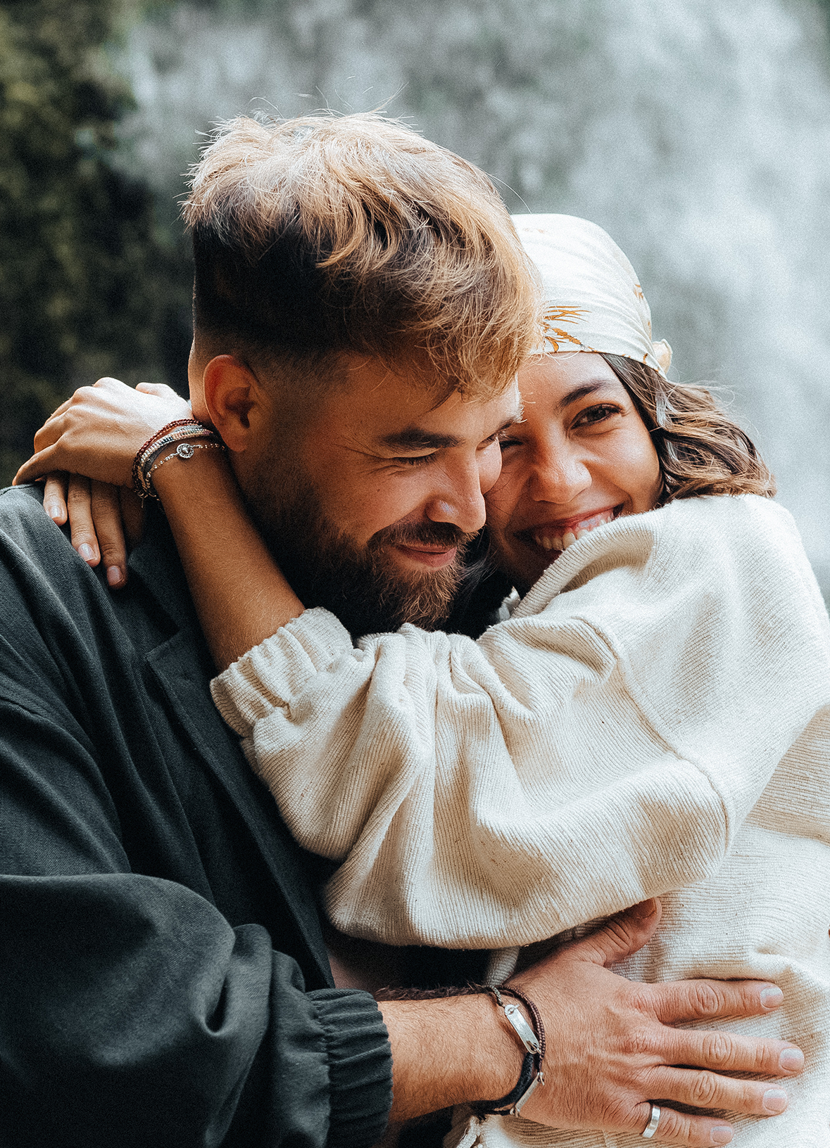 A couple embracing and smiling near a waterfall backdrop.