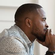 Side profile of a Black man with a beard, resting his chin on his hand in thought.