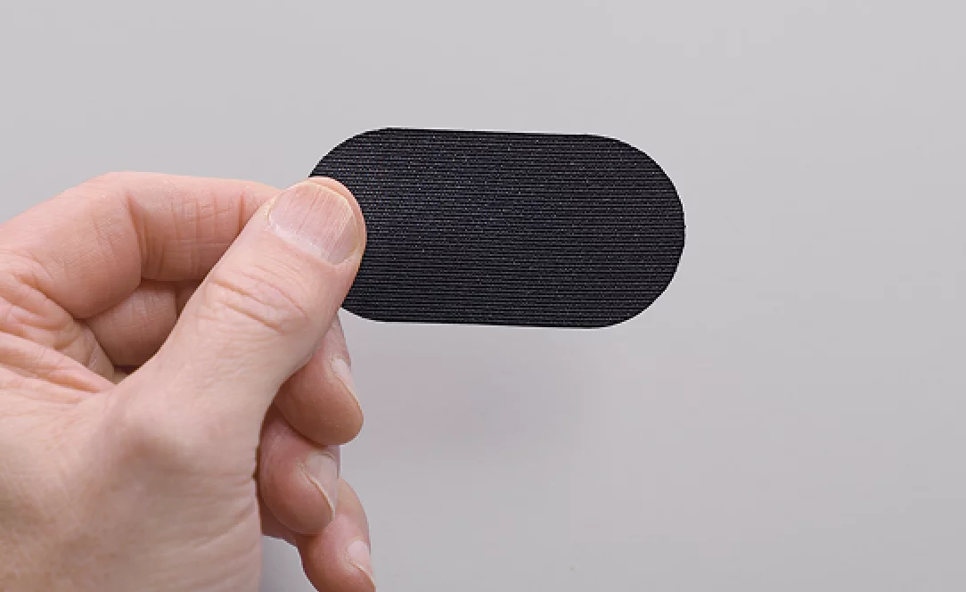 Hand holding a small black oval item against a plain background.