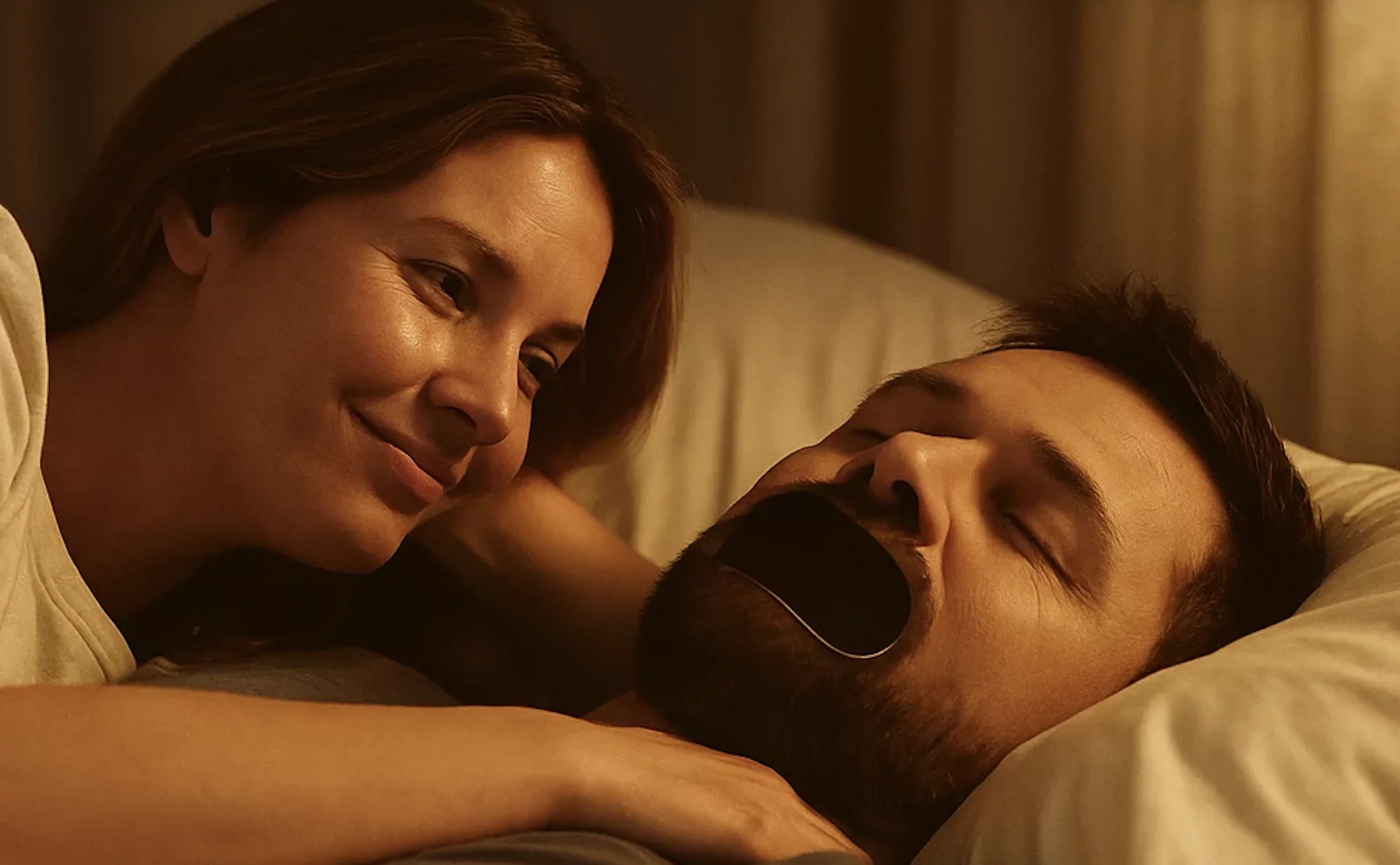 Woman smiling at man with mouth taped, lying in bed.