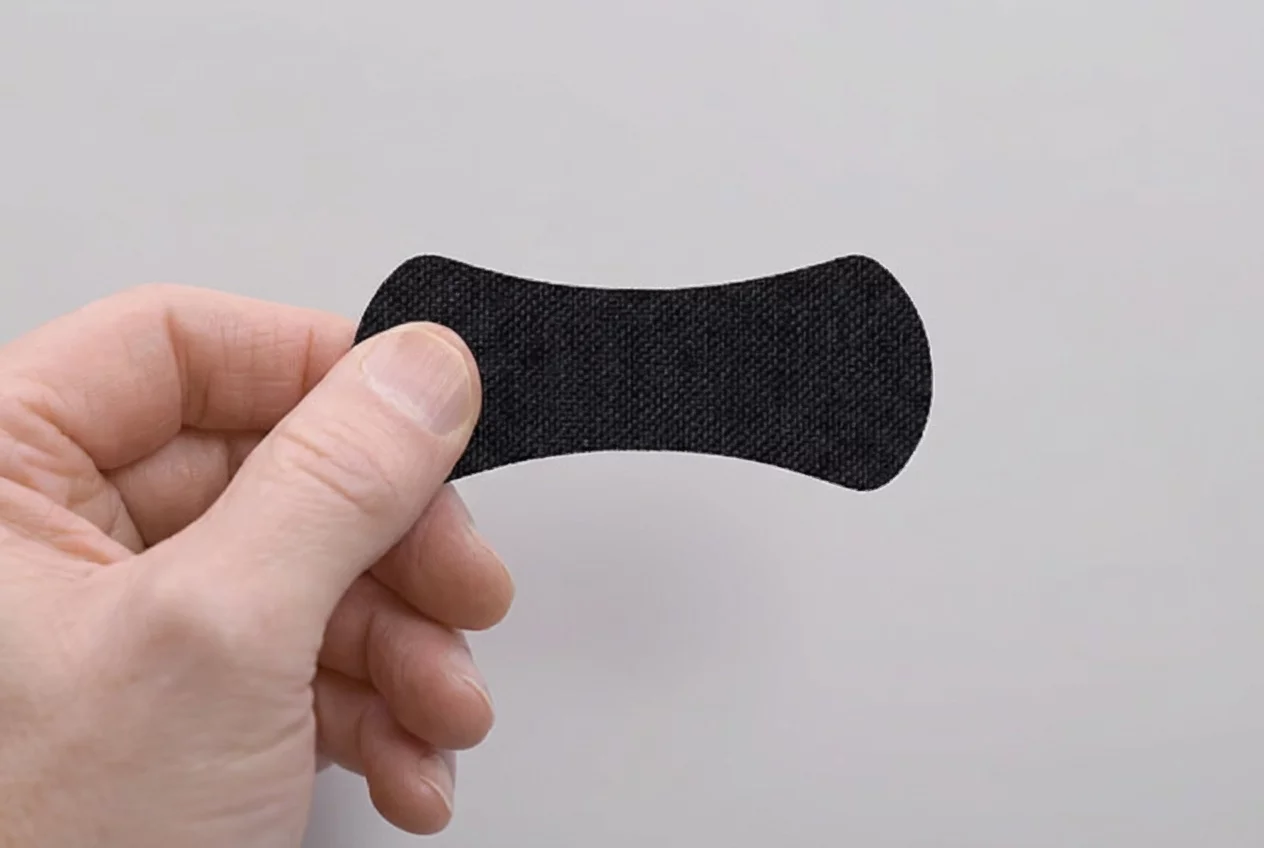 Hand holding a small black oval item against a plain background.