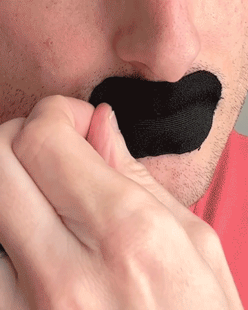 Person peeling black tape off their lips.