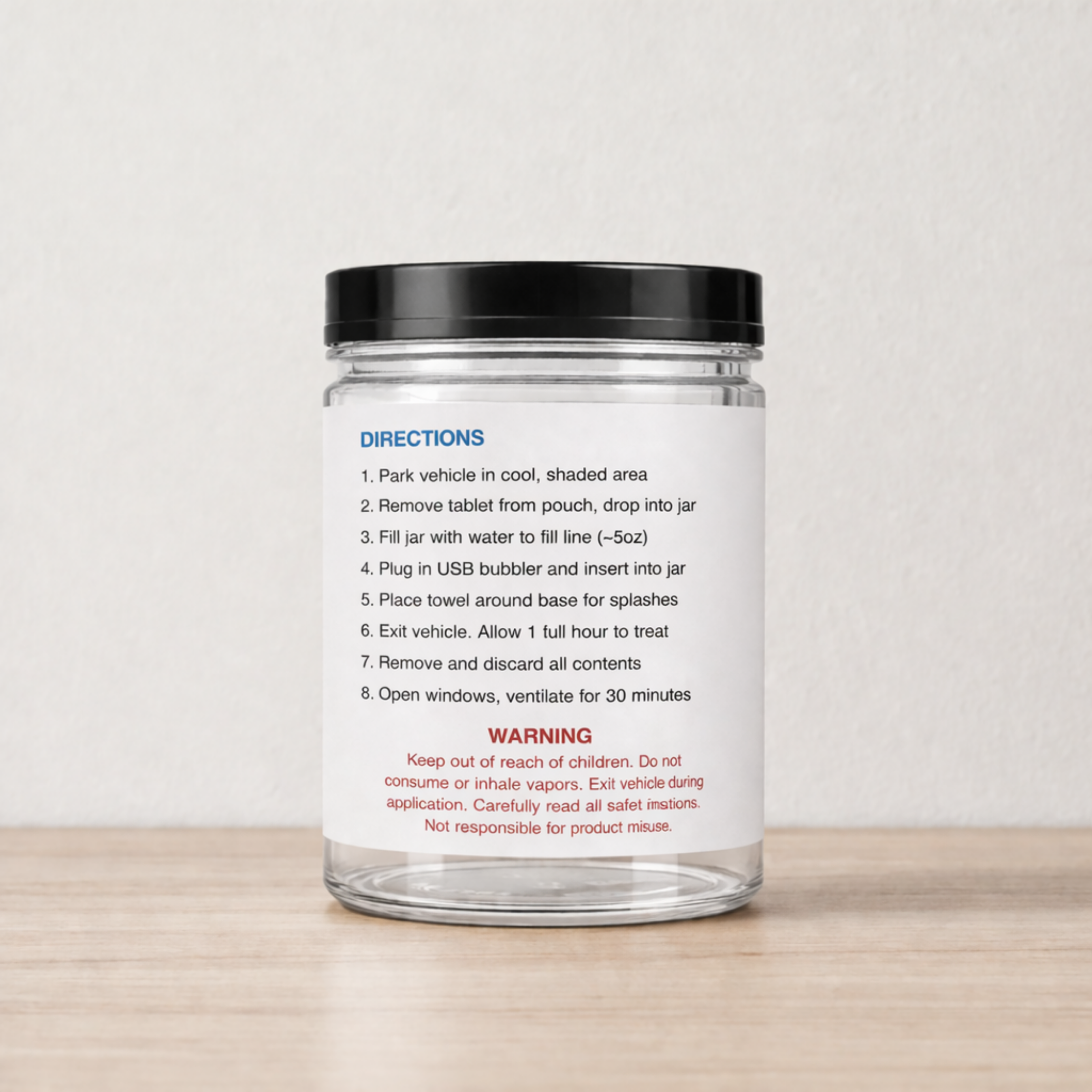 A clear glass jar with a black lid sits on a wooden surface, showing a directions and warning label.