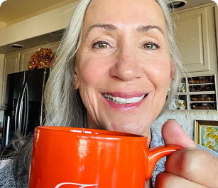 Smiling person holding an orange mug in a kitchen.