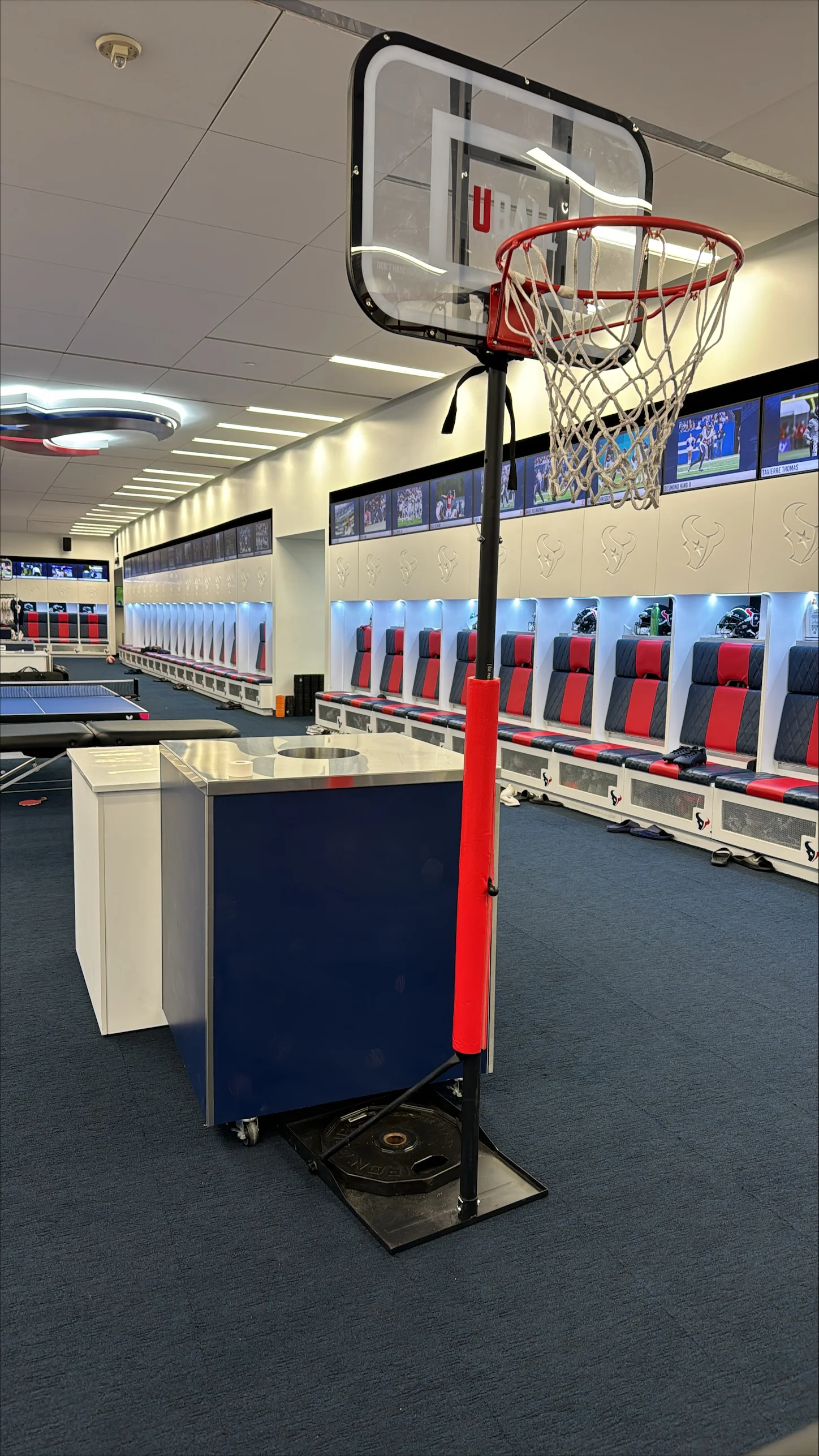 Locker room with a basketball hoop and red-blue seating.