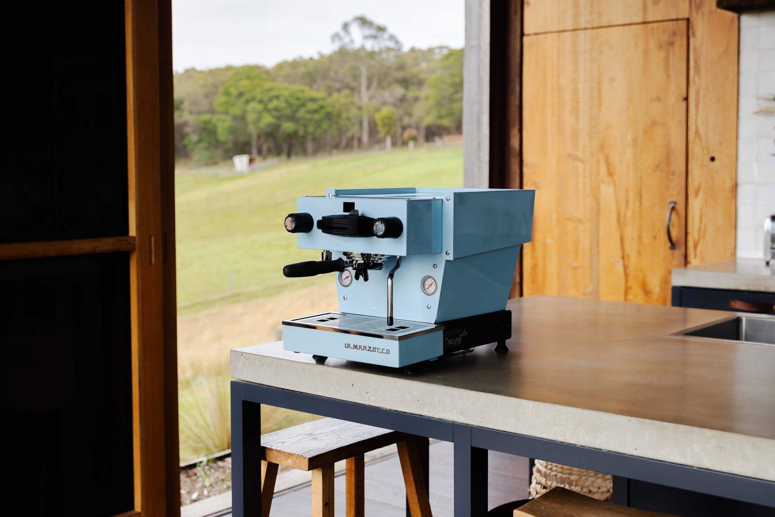 Blue espresso machine on a countertop with a scenic outdoor view.