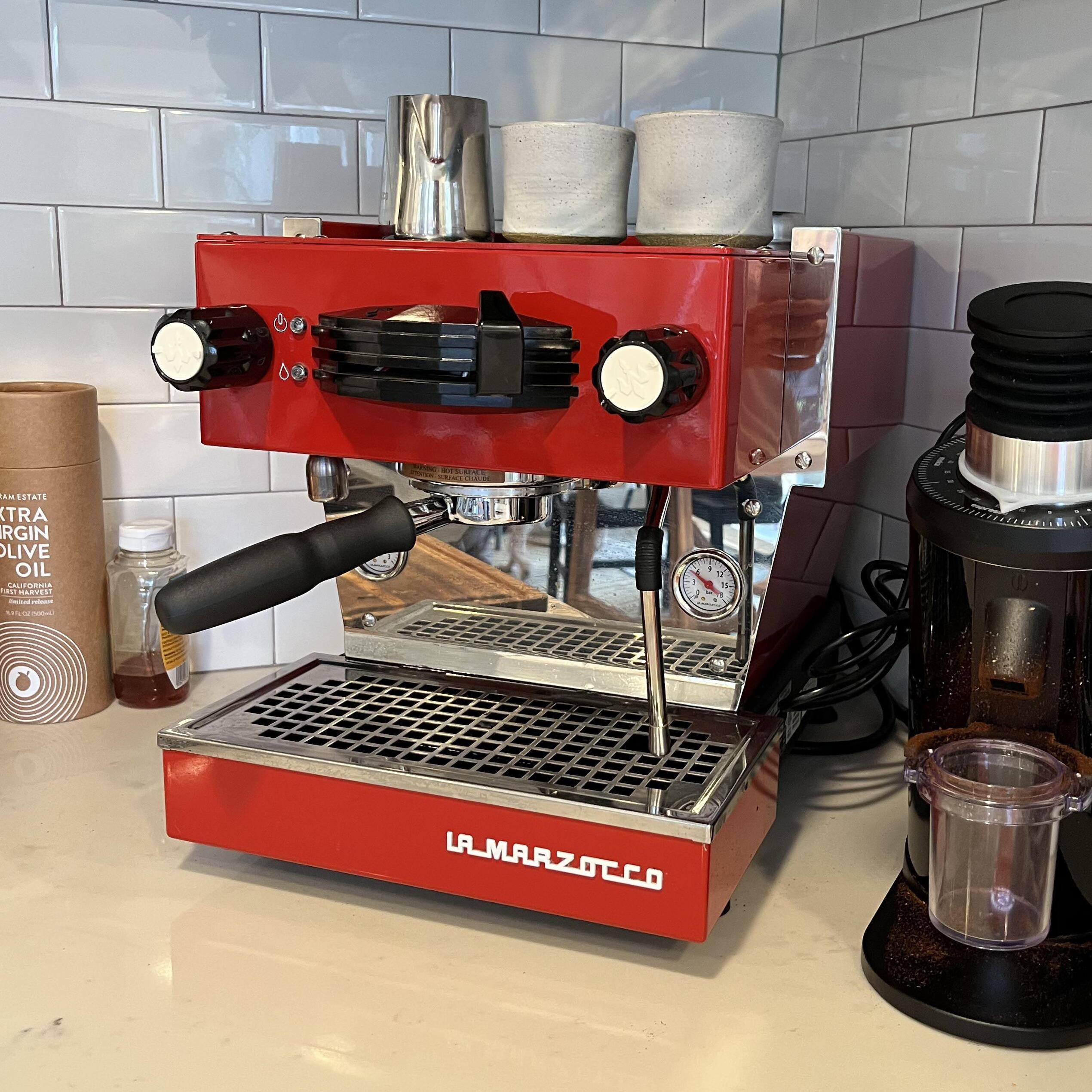 Red espresso machine on a kitchen counter with cups on top.