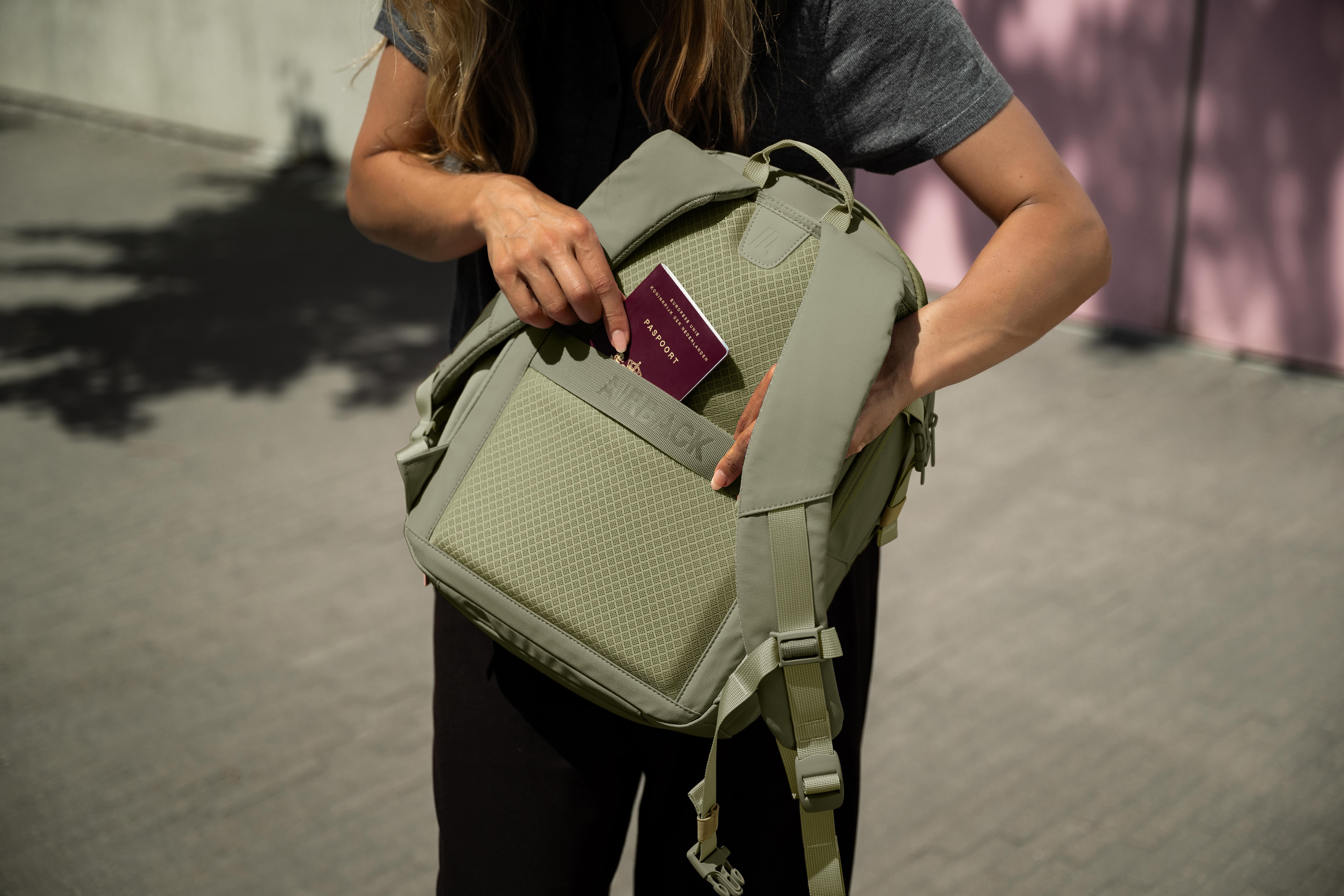 A person puts a passport into a pocket on the back of a light green backpack.