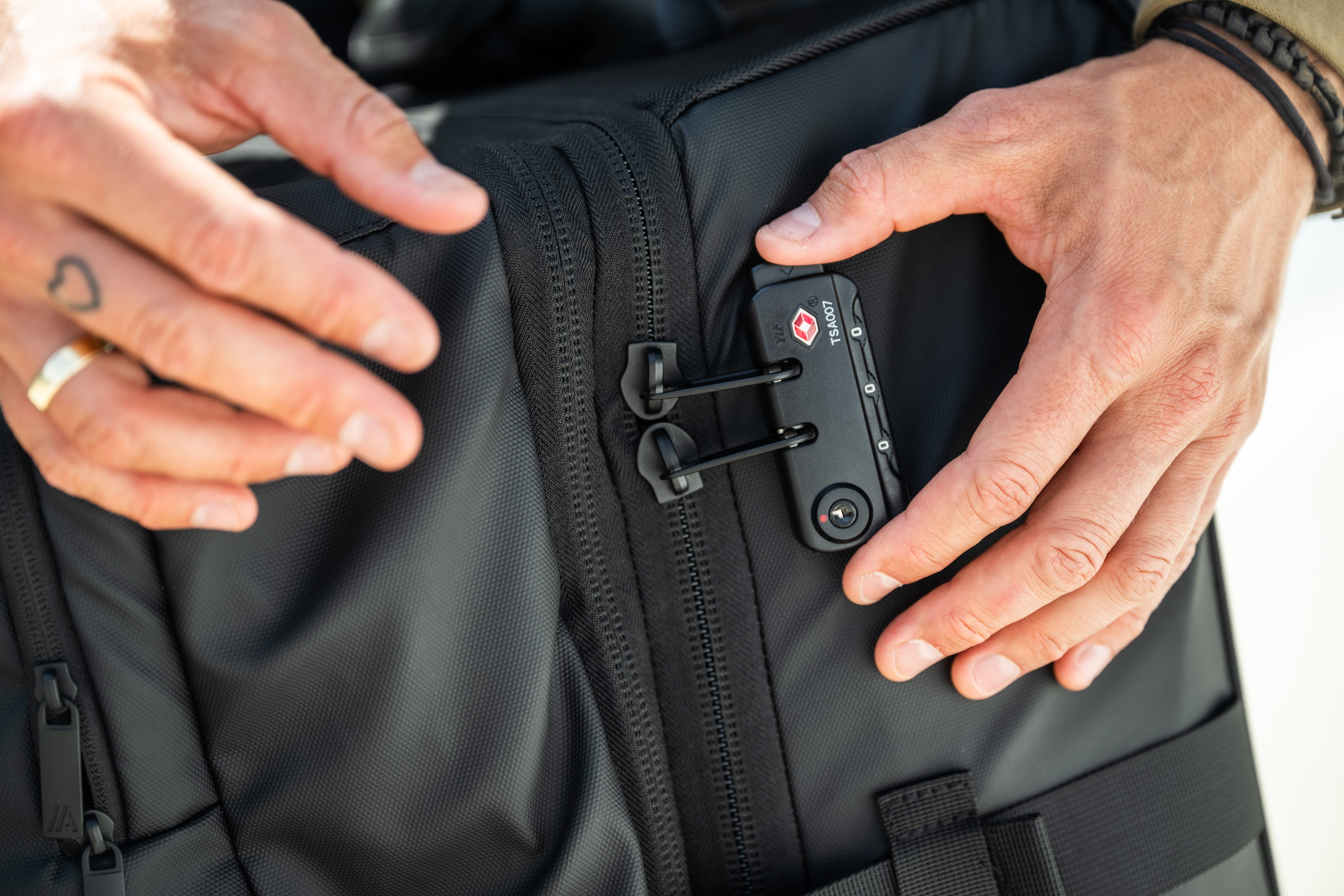 A close-up of hands locking a black backpack with a TSA-approved combination lock.